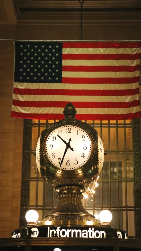 an iron clock sitting underneath a flag in front of a station