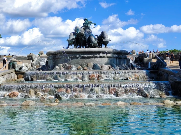 the fountain is at the edge of the park, while people walk along the path