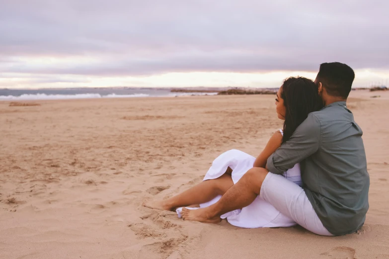 the man and woman are sitting down on the beach