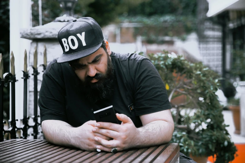 a man with a beard and wearing a hat while using his cellphone