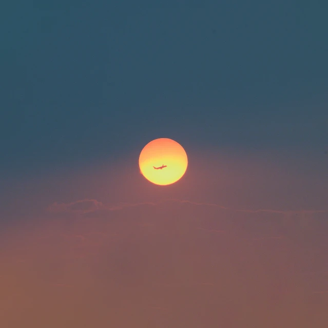 an airplane flying in front of the sun on a hazy day