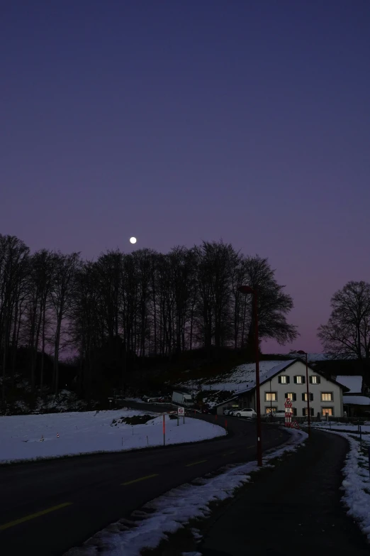 a dark, snowy road and a house with lights on