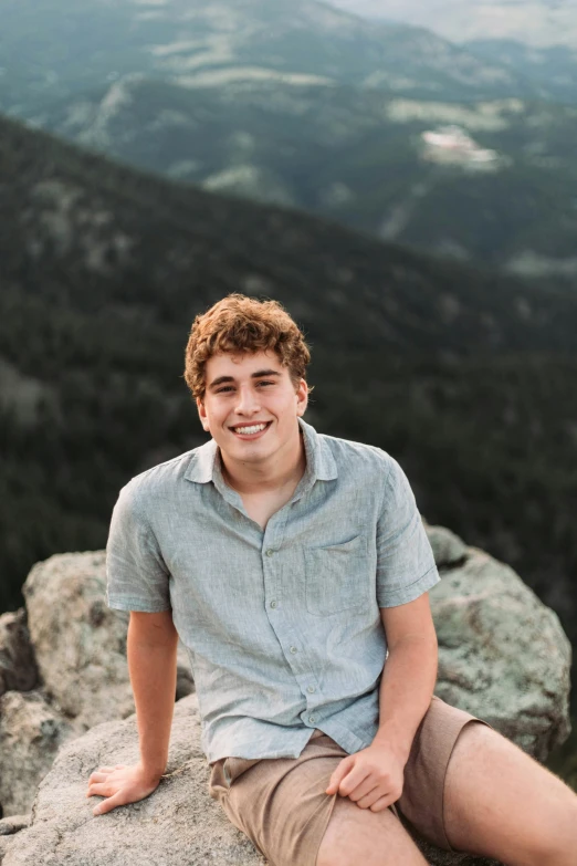 a boy sits on a large rock and smiles at the camera