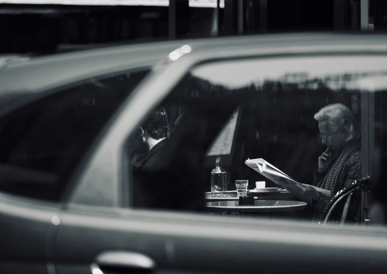 a man is reading a book while another person sits at a table in the background