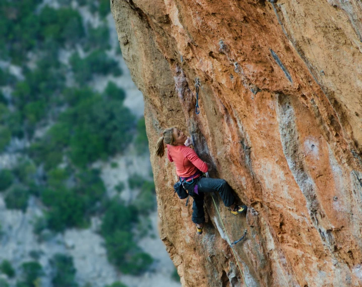 a man with orange shirt climbing up the side of a cliff