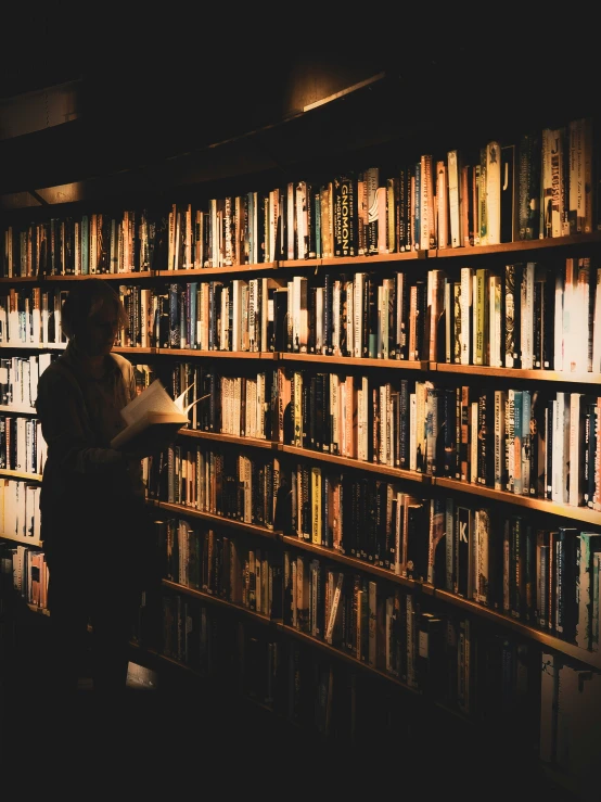 a person sits in front of a book shelf in a dark room