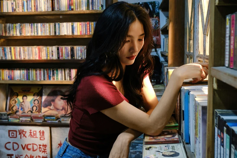 an asian woman standing near the shelves of dvds