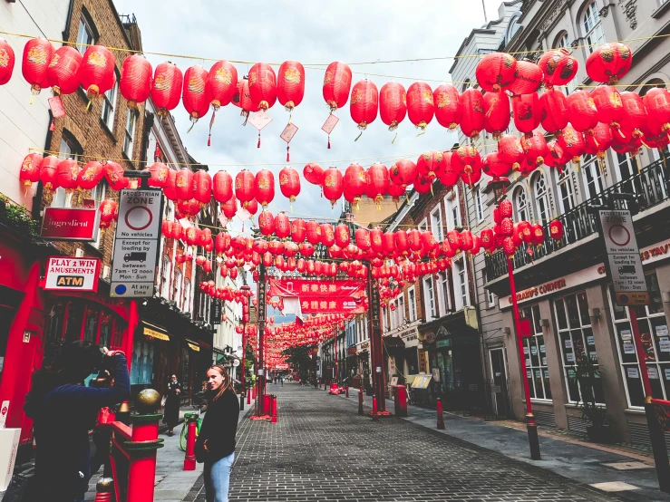 a street full of people holding flags, with red chinese paper lanterns hanging above them