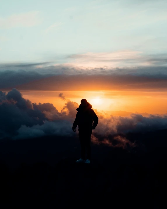 the silhouette of a person standing on a hill watching the sun