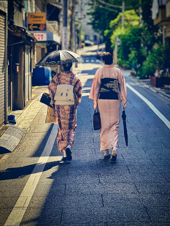 two people with umbrellas walk down a street on a sunny day