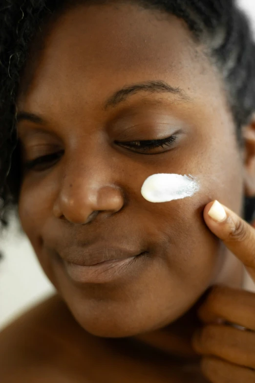 a woman with one eyeliner on applying cream on her cheek