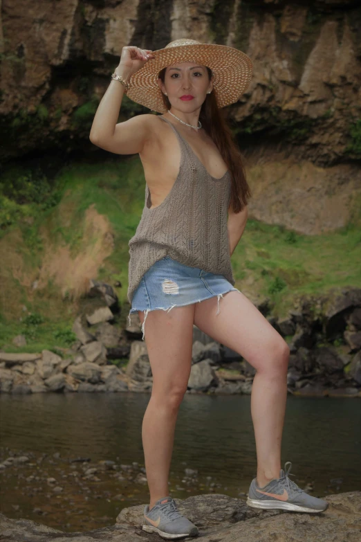 a woman with a hat standing on rocks near water