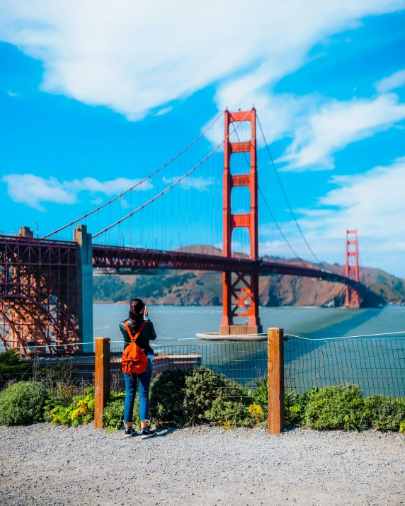 two people are standing on a rock looking at the water and a large bridge