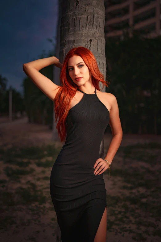 a woman in black posing for a picture next to a tree