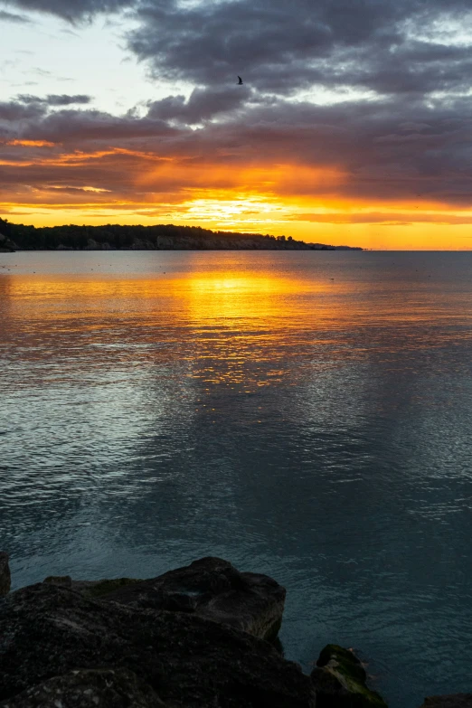 a sunset over a body of water with rocks on the shoreline