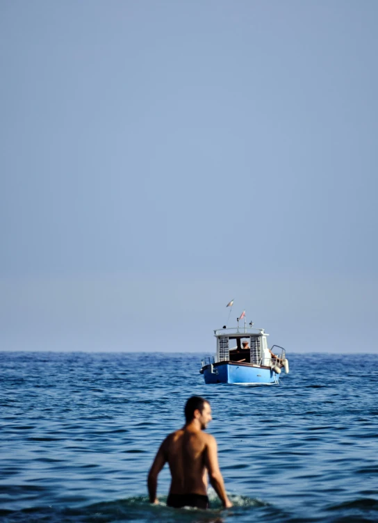 man wading in the ocean with a boat behind him