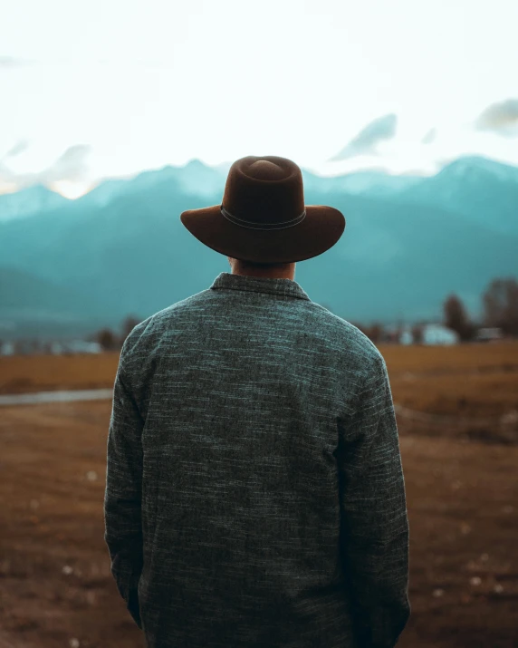 a man with a cowboy hat standing in front of the mountains