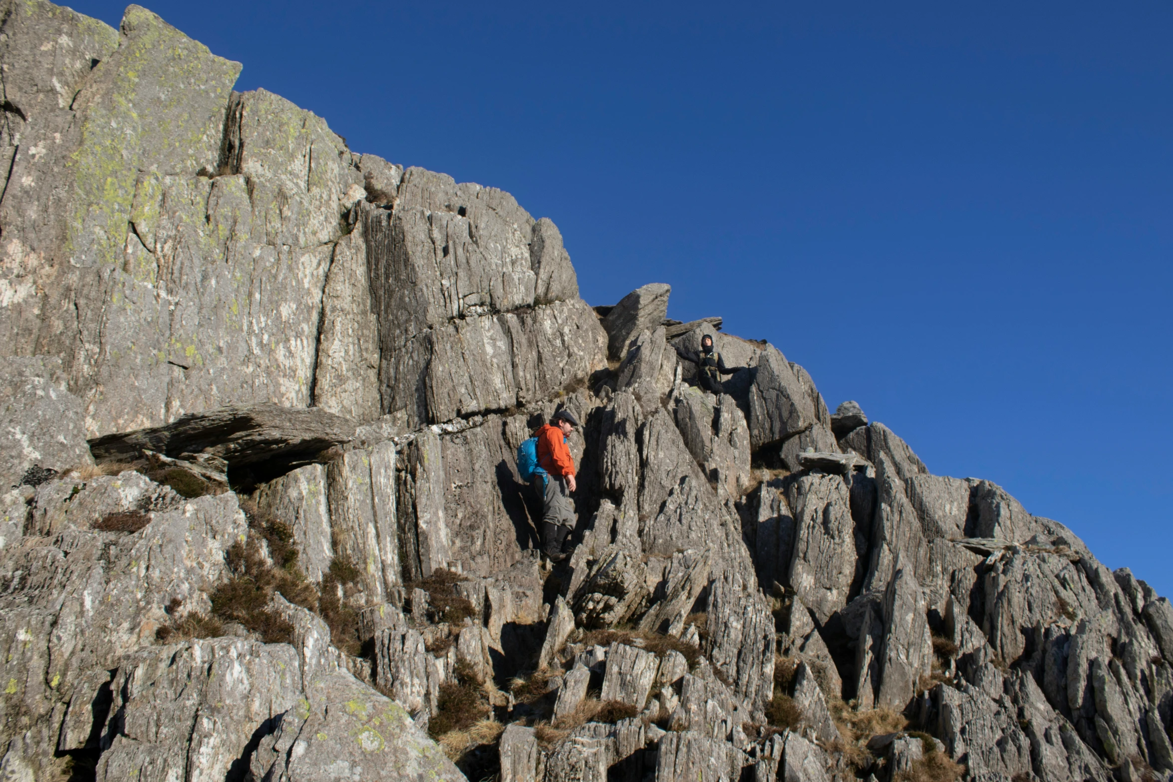 two people climbing a rocky cliff in the mountains