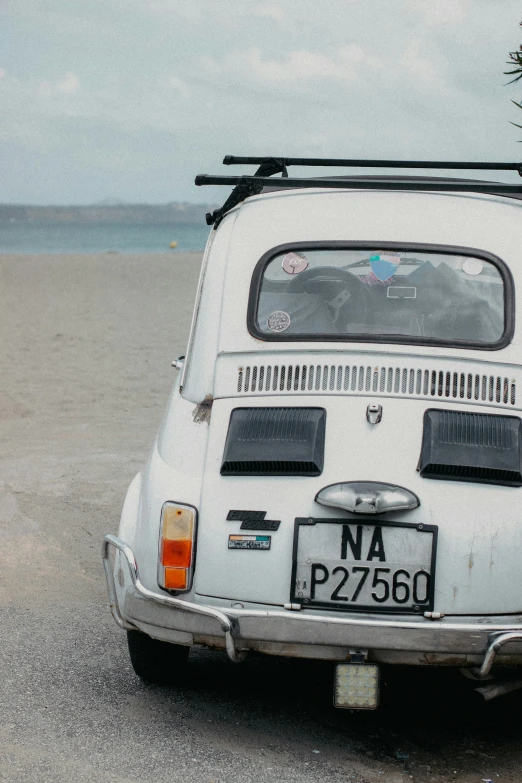 an old white vehicle sitting in the sand on a beach