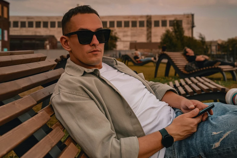 a man in sunglasses sitting on a park bench looking at his phone