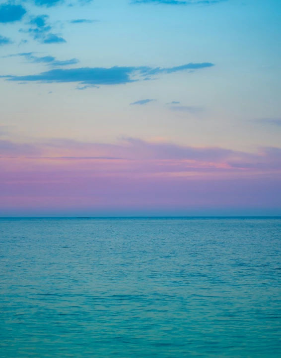 a lone boat floating in an ocean at sunset