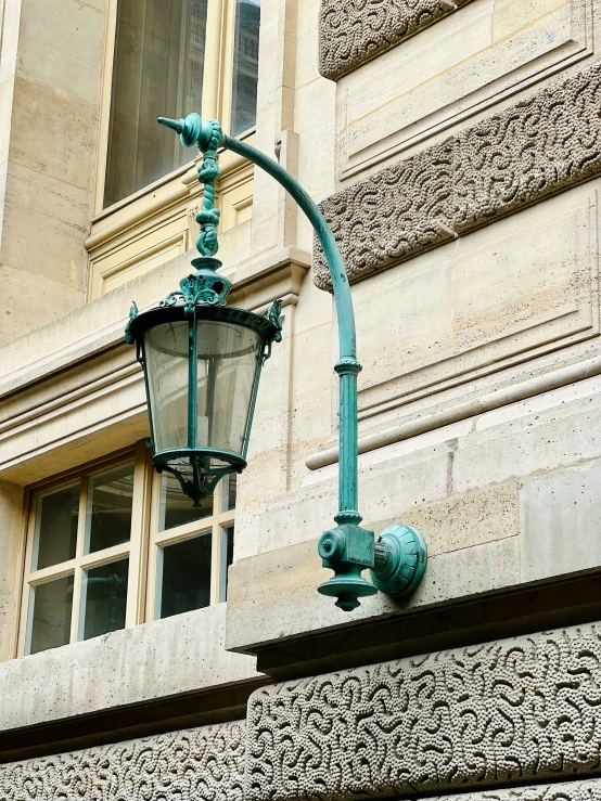 an ornately decorated green lamp stands on the outside of a stone building