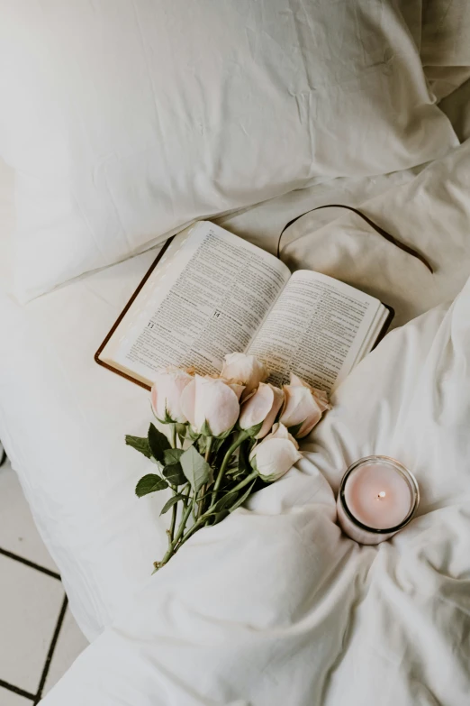 an open book with a candle and flowers on a white blanket