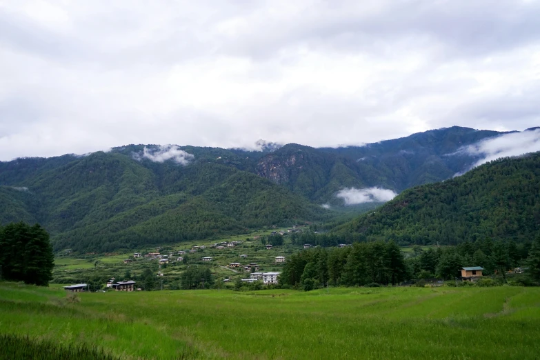 a green mountain covered in clouds with a lot of houses