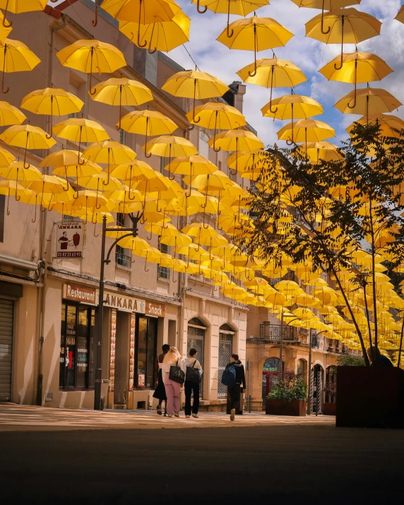 people are walking on a city street in the rain with yellow umbrellas hanging from them