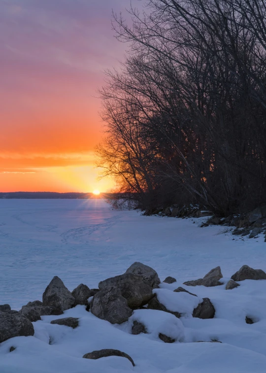 sunset over a frozen landscape and rocks in front of the water