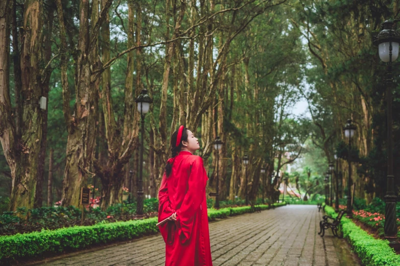 woman in red dress looking up into tree lined path