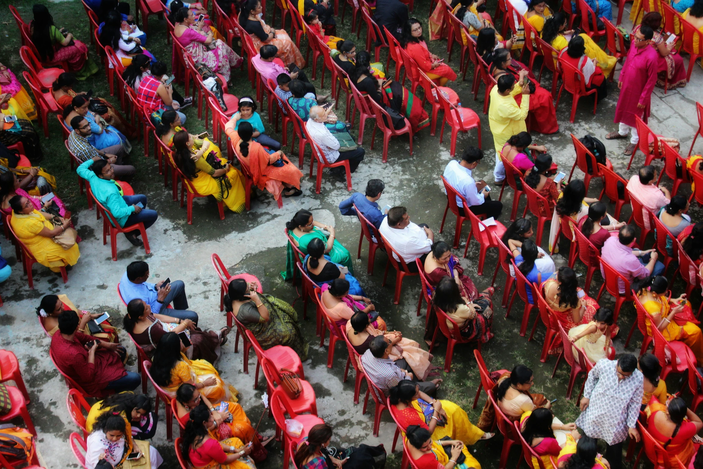 large crowd sitting around bright red plastic chairs