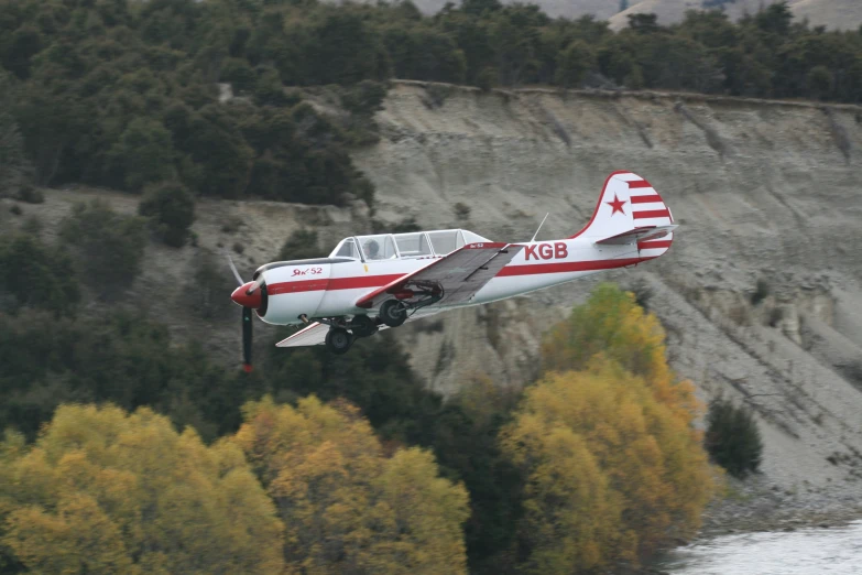 an old aircraft flies over a river and a large mountain