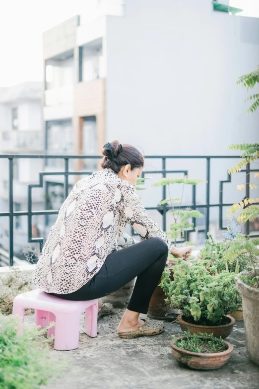 a woman sitting on a stool next to several potted plants