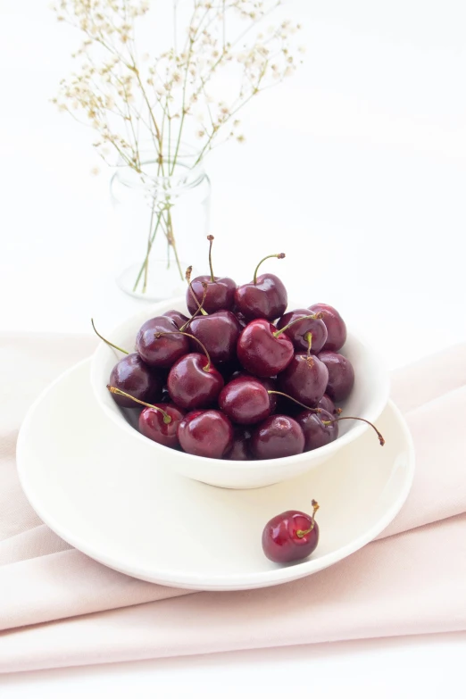 a bowl of plums is sitting next to some flowers