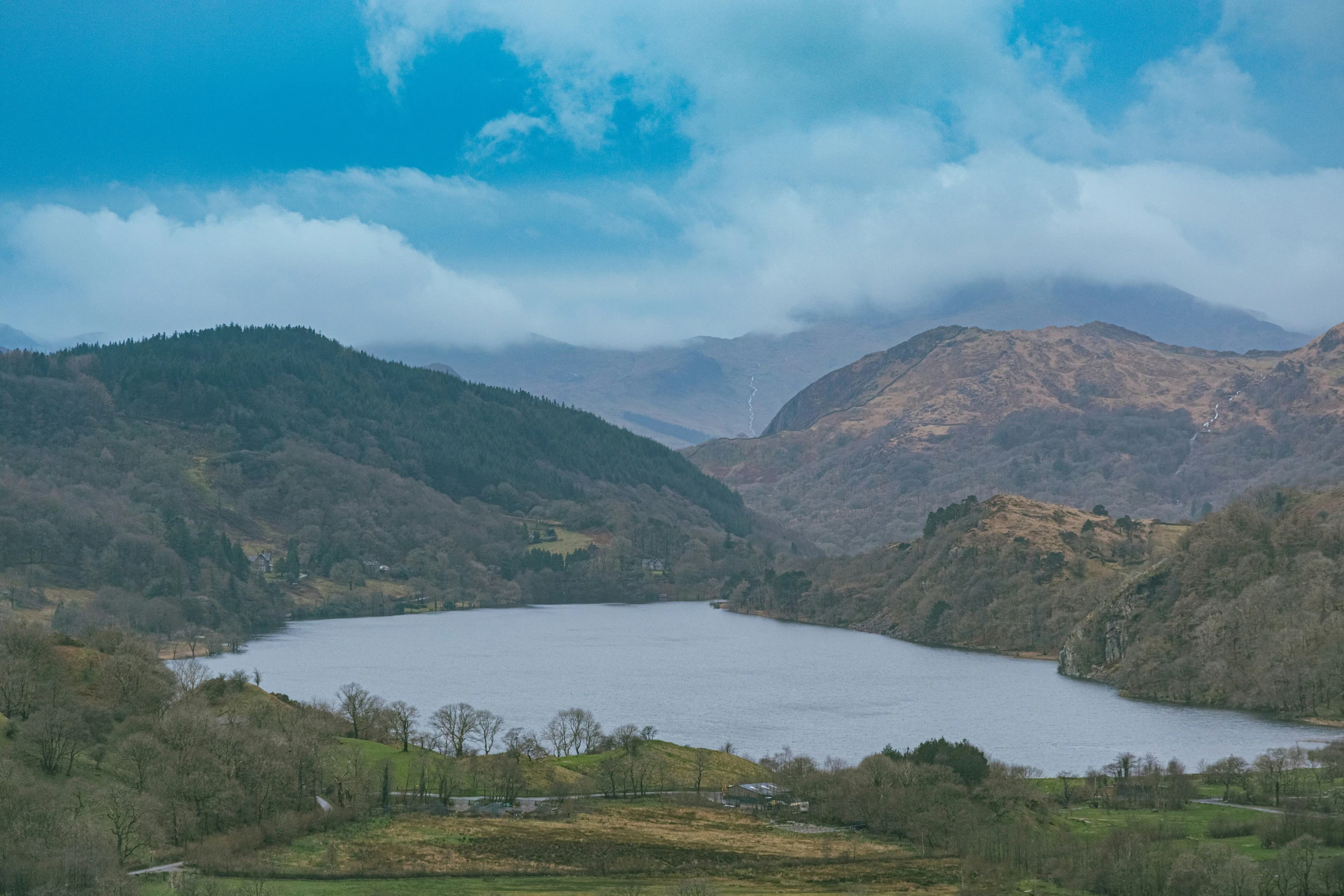 a lake surrounded by mountains under a cloudy sky