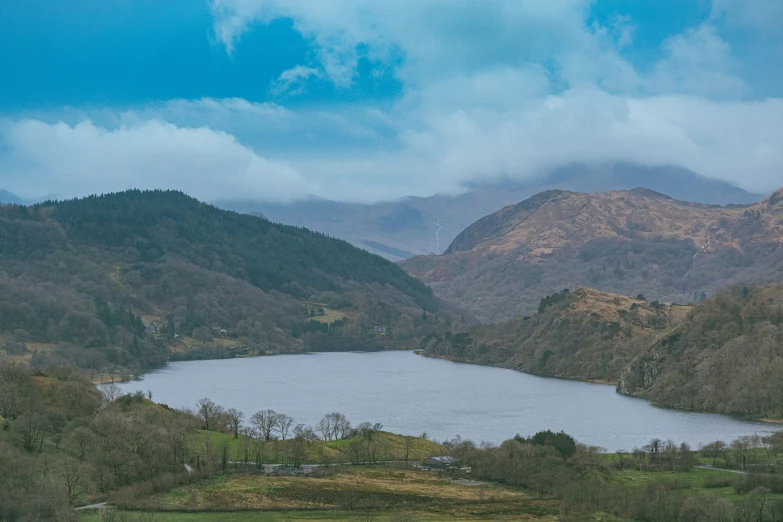 a lake surrounded by mountains under a cloudy sky