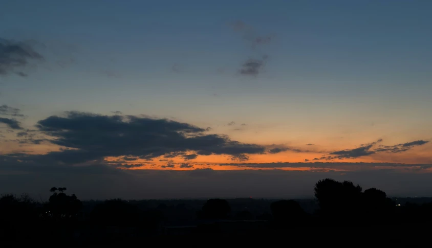 the sun is setting in a distant sky over trees