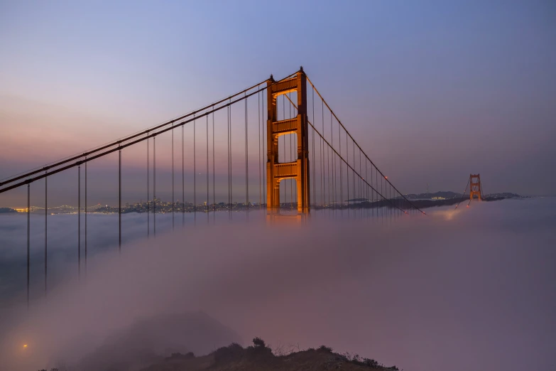 a suspension bridge with fog on the ground