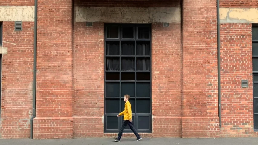 a man in a yellow shirt is walking by a brick building