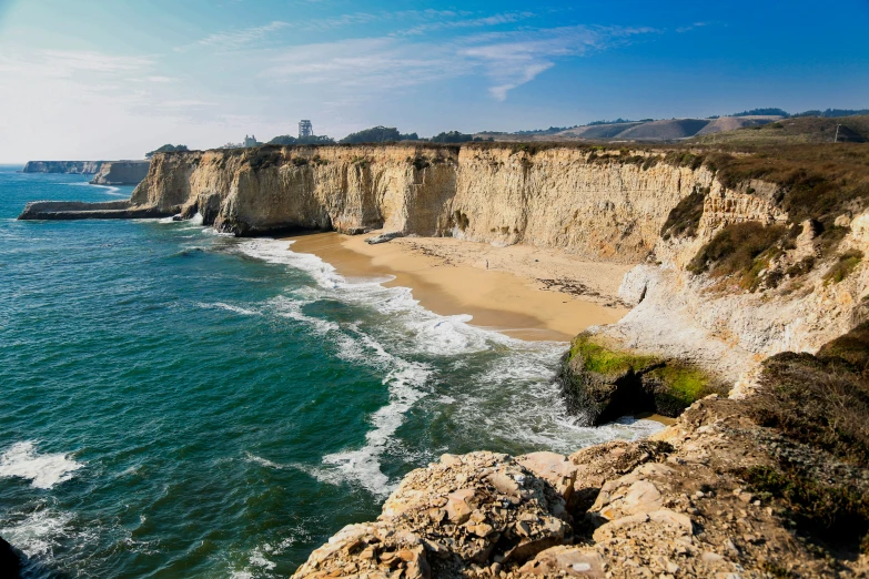 a cliff on the shore of the ocean with waves crashing up the beach