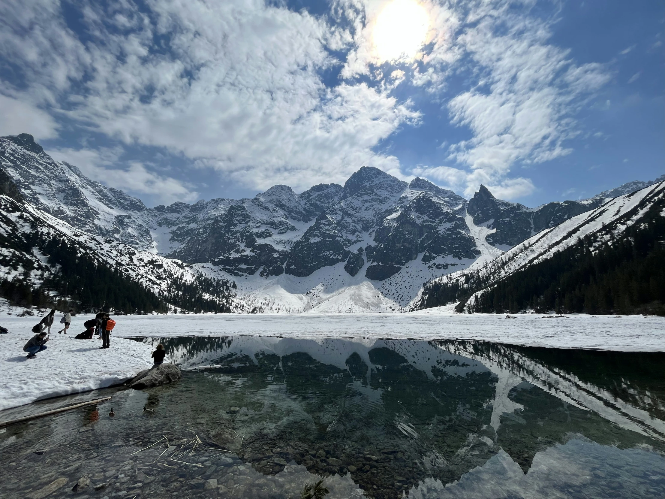 people are standing by the edge of a lake and snow mountains