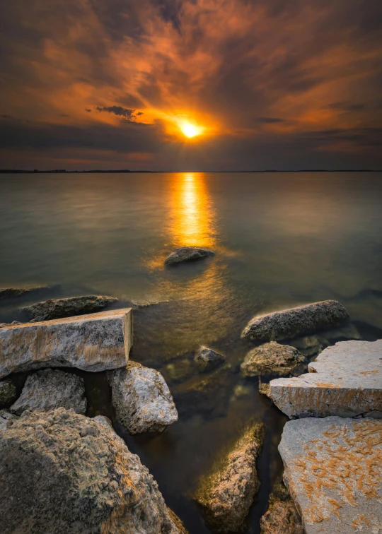 the sun is setting over some rocks in the water