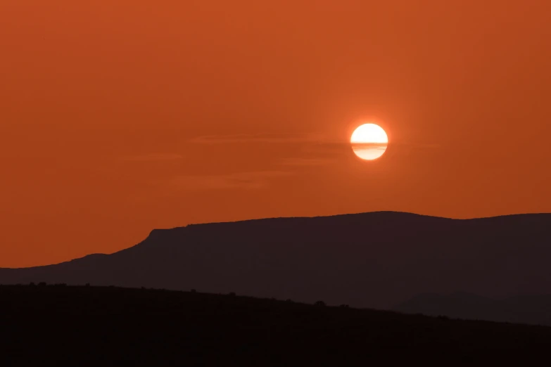 the sun setting over a mountains covered in orange hues