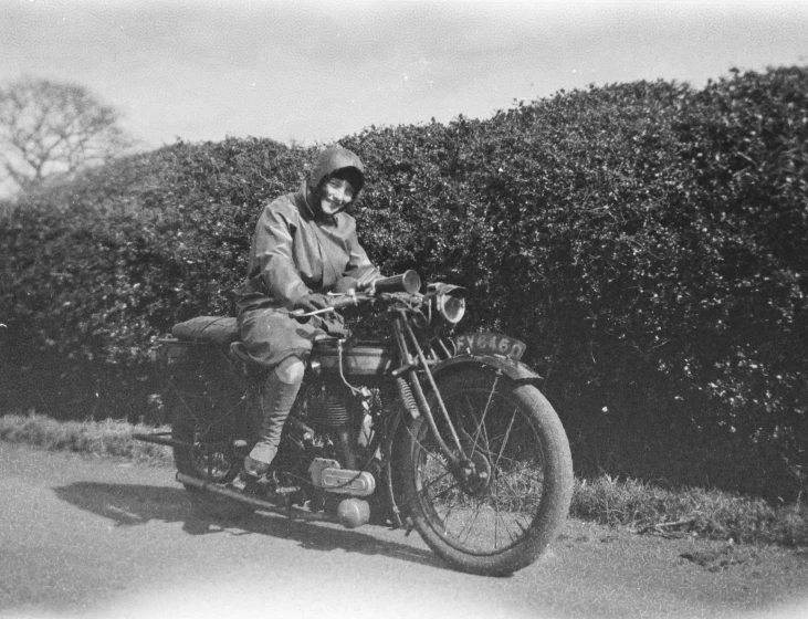 a man sitting on a motorcycle in front of hedges