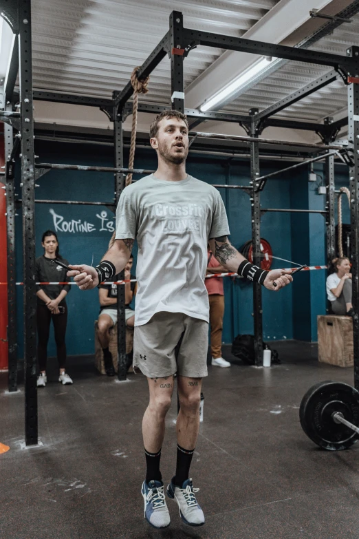 man with arms up and a hand in his other arm while standing near barbells in a crossfit gym