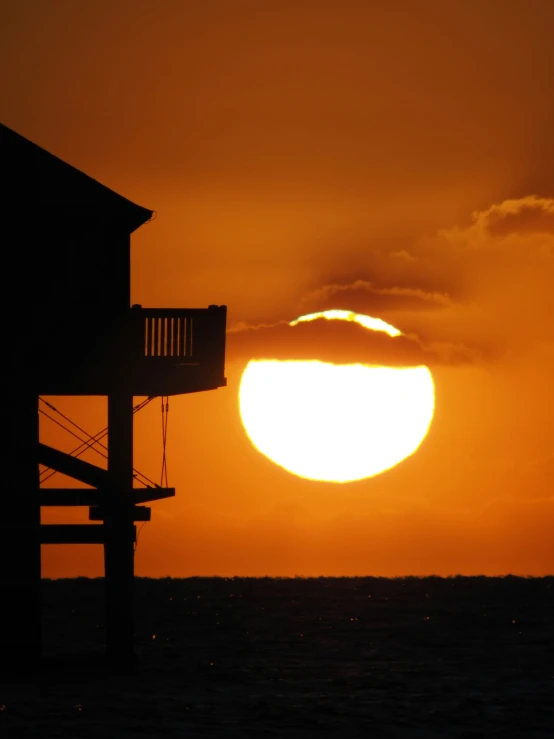 the sun is setting over the ocean with a building on it