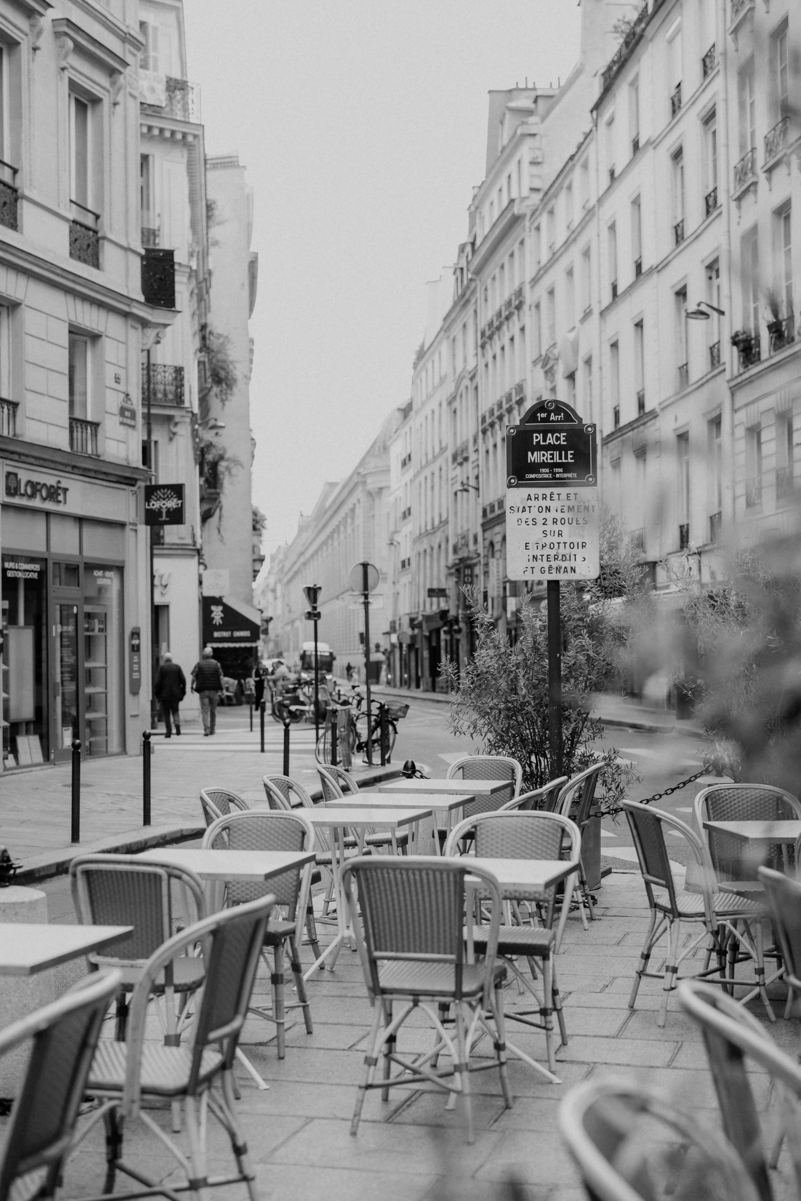 a black and white pograph of tables and chairs on a busy city street