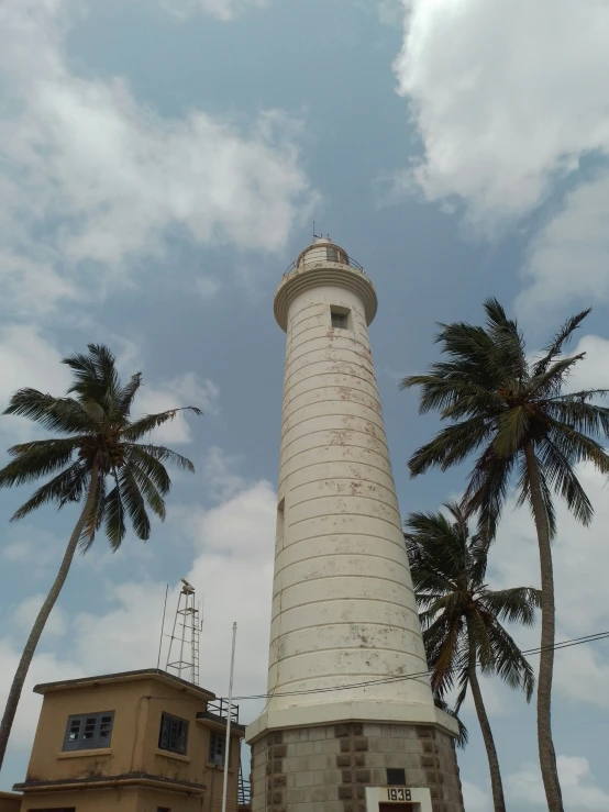 the white lighthouse is on top of some palm trees