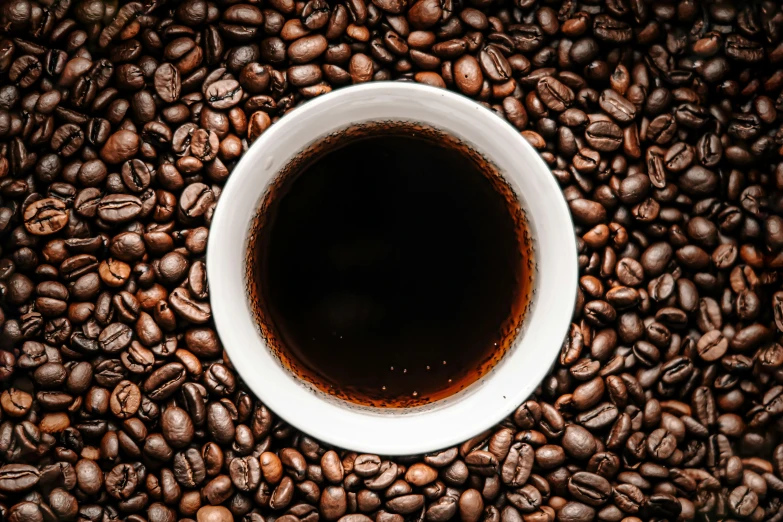 a cup of coffee sitting in the middle of roasted beans